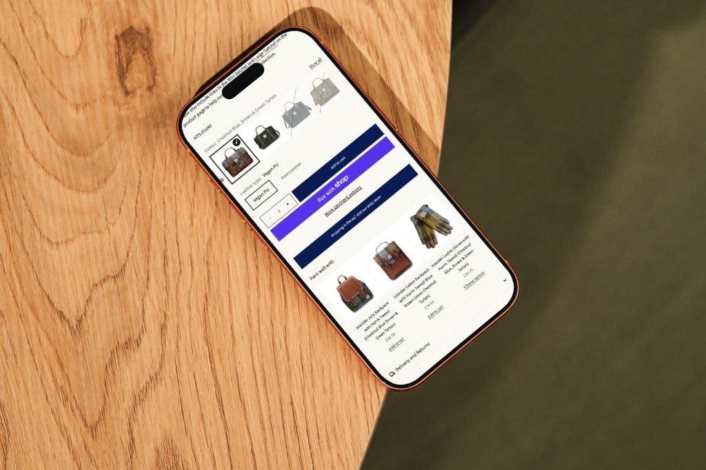 A phone on a wooden table showing a Harris Tweed satchel, with colour, quantity and buy buttons