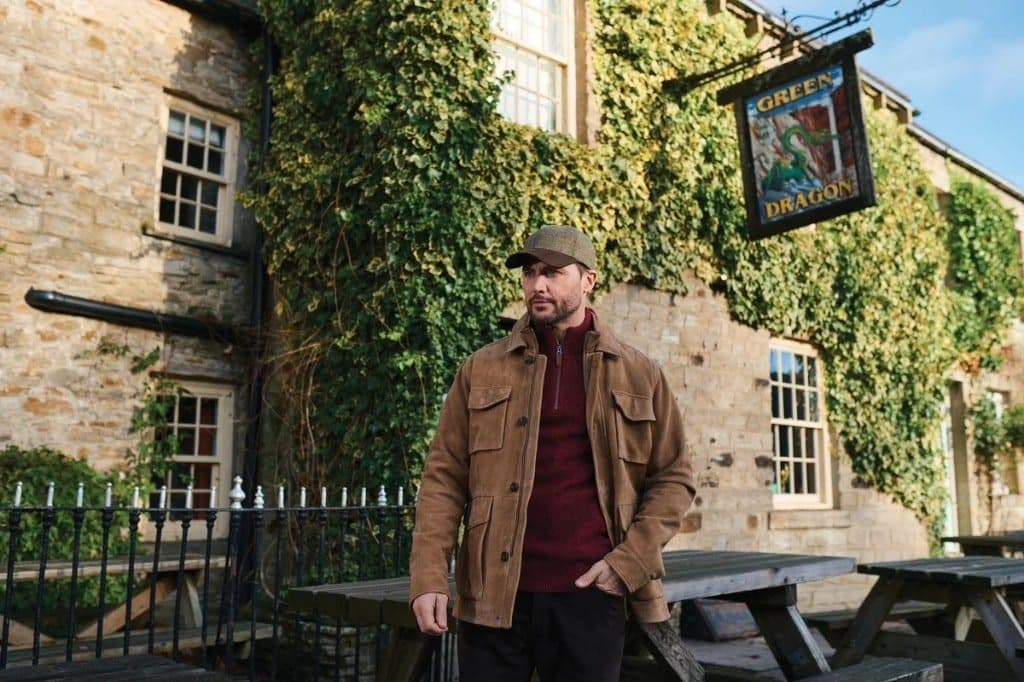 A man in a Harris Tweed jacket and flat cap outside the Green Dragon, with ivy covering the stone wall